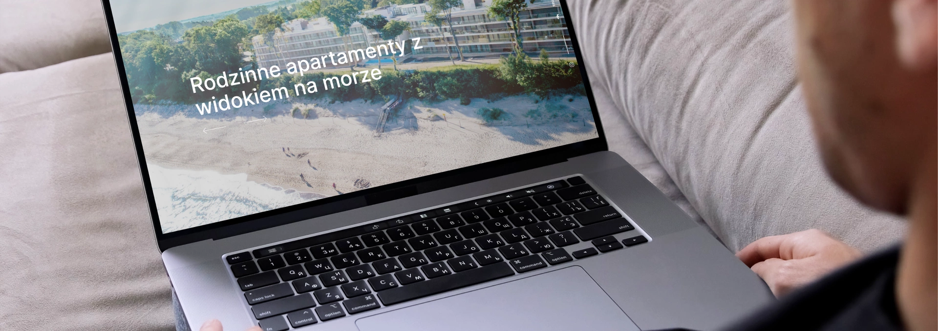 Osoba przegląda stronę Hevenia na laptopie. Ekran wyświetla hasło „Rodzinne apartamenty z widokiem na morze” oraz zdjęcie plaży otoczonej zielenią.